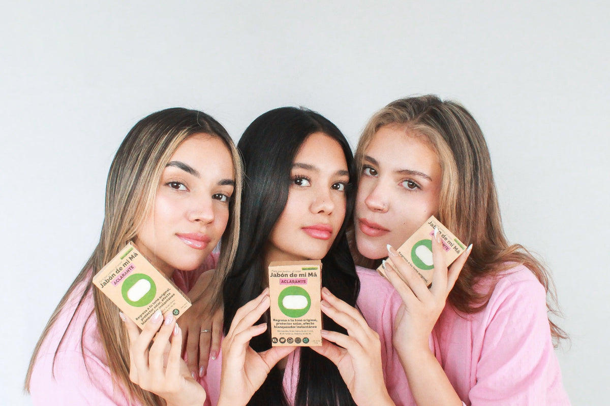 Tres mujeres jóvenes sosteniendo cajas de Jabón de Mi Má Aclarante.